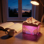 3D mountain lamp on a desk with an open book and coffee cup, window view in the background